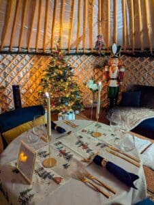 The yurt is all ready for a romantic private dining experience for 2 with the private chef. The tablet is set for Christmas with a table runner adorned with Christmas trees, in the distance is a Christmas tree with warm yellow lighting and a large full sized nut cracker.