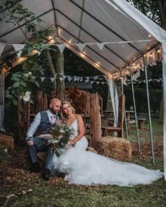 A bride and groom in an embrace on haybales under the woodland marquee, an intimate, elopement wedding for 2.