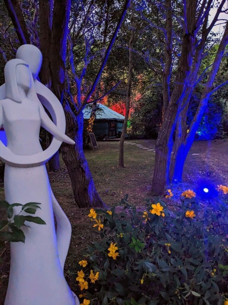 Statue of a couple in an embrace with the yurt for private dining and couples massages woodland beyond.