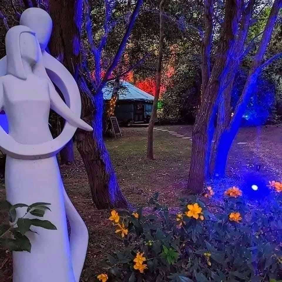 Romantic woodland scene at Hawthorn Hideaway on the Chesterfield Canal, featuring an abstract sculpture of embracing figures, blooming spring flowers, and glowing trees — a magical outdoor setting for Valentine’s breaks and couples’ retreats in Yorkshire.