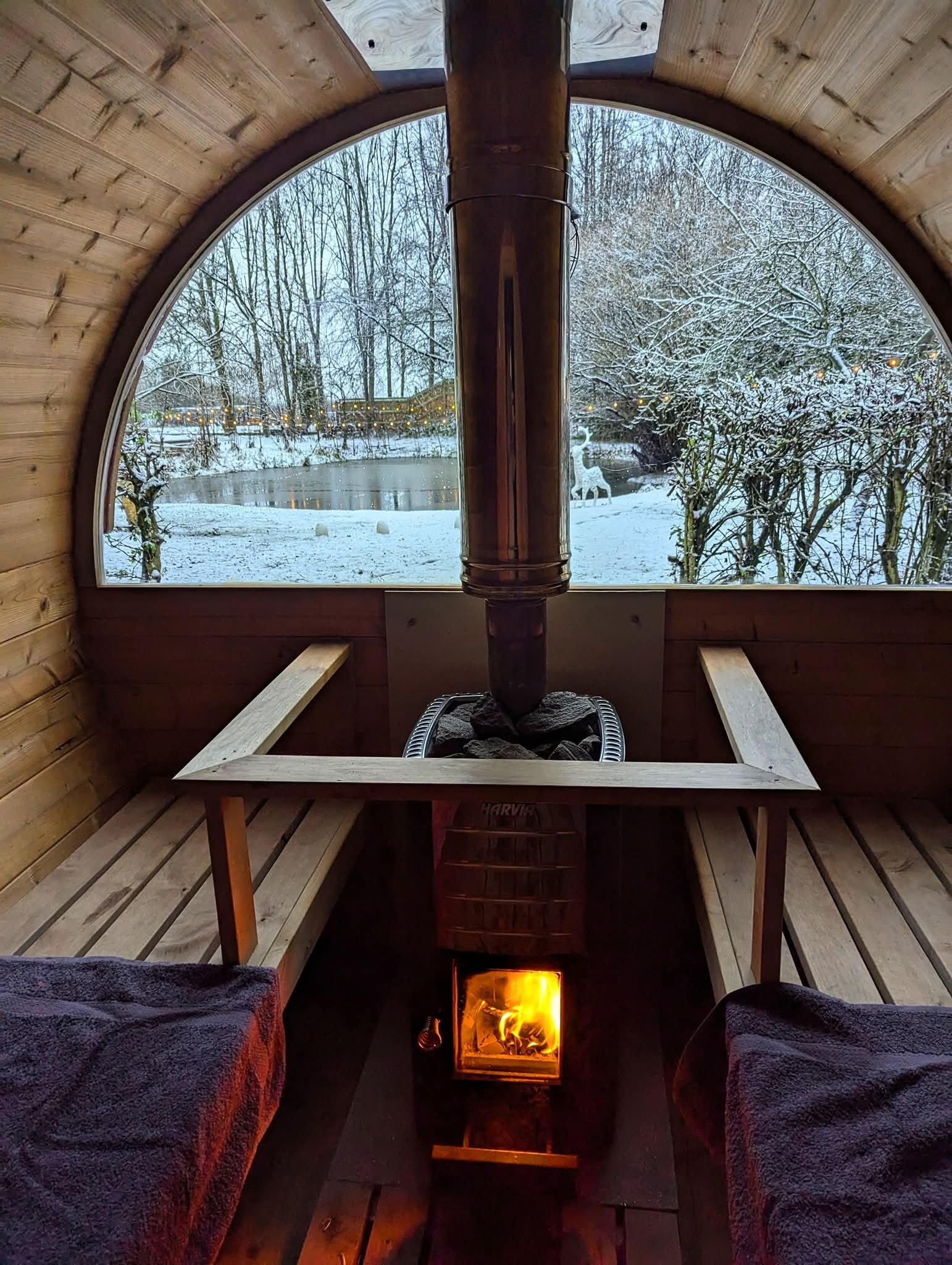 The wood burning sauna with cosy flames and a woodland and duck pond in the distance covered in snow for romantic winter getaways near me on the Yorkshire border.