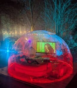 A cosy, romantic night time scene for UK honeymoon escapes, A geodome cinema experience set in a rainbow woodland garden, magical and private.